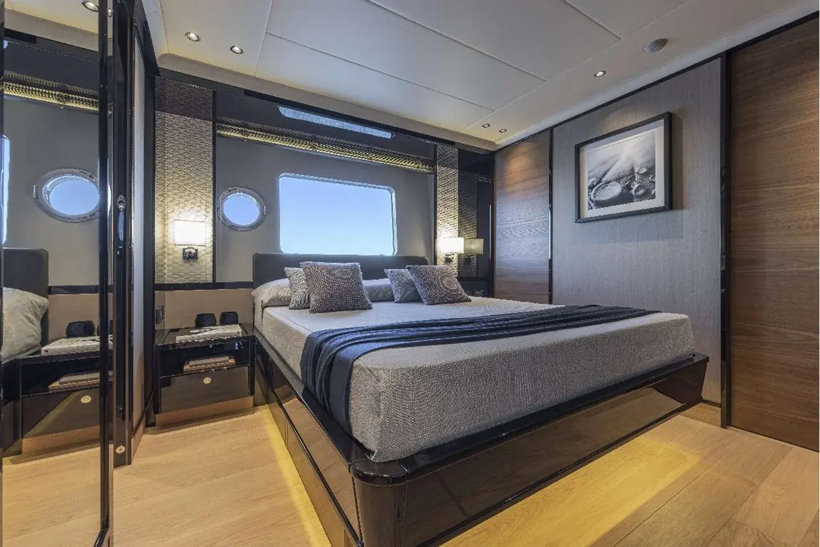 Luxury yacht interior featuring a modern bedroom with a large bed, two pillows, and round windows allowing natural light.